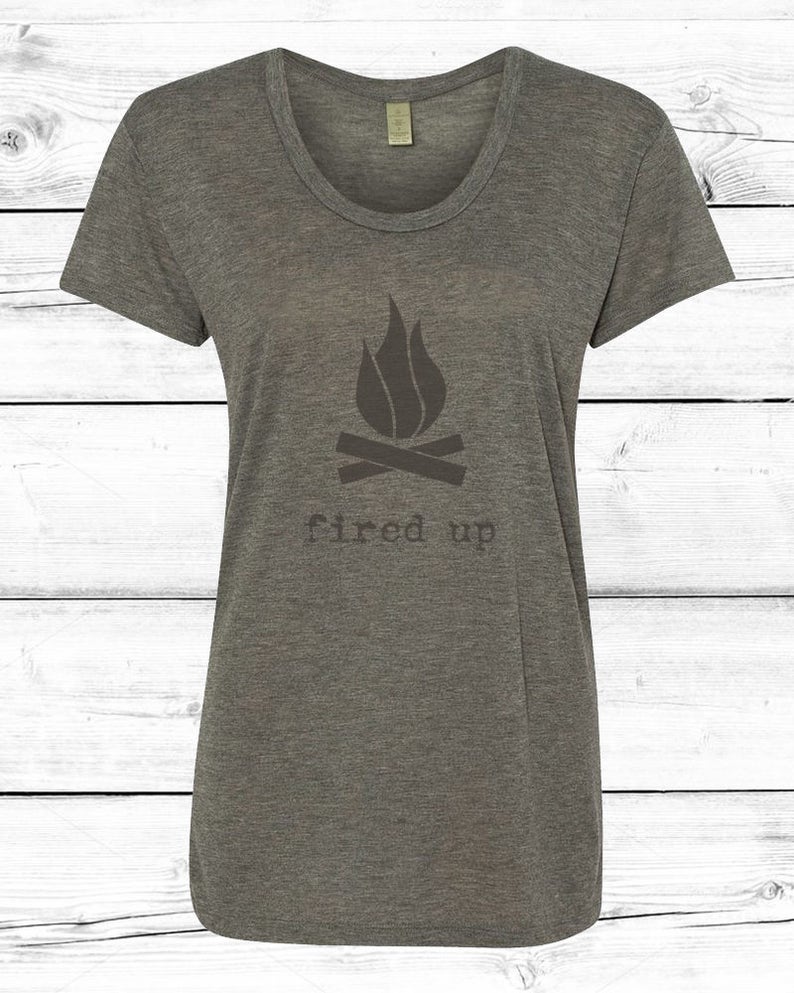Puede incluir: Una camiseta gris jaspeado con cuello redondo con un gr&aacute;fico de fogata. El gr&aacute;fico incluye un dise&ntilde;o de llama sobre dos troncos cruzados, con las palabras "fired up" impresas debajo en una fuente sencilla. La camiseta es de material suave.
