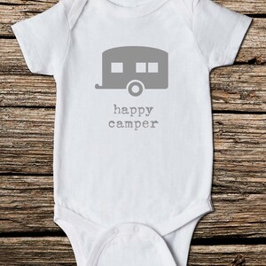May include: White baby onesie with a gray camper graphic and the words "happy camper" printed below. The onesie is made of soft material and has short sleeves. Perfect for a baby.