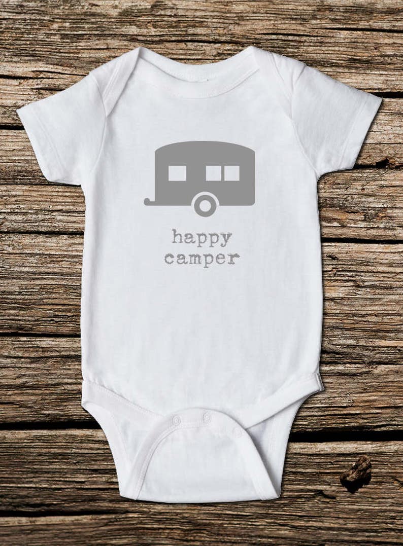May include: White baby onesie with a gray camper graphic and the words "happy camper" printed below. The onesie is made of soft material and has short sleeves. Perfect for a baby.