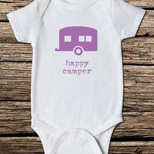 May include: White baby onesie with a purple camper graphic and the words "happy camper" printed below. The onesie is made of soft material and has short sleeves. Perfect for a camping-themed baby shower or as a gift for a new parent.