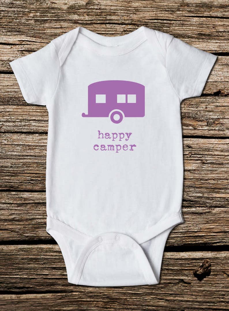 May include: White baby onesie with a purple camper graphic and the words "happy camper" printed below. The onesie is made of soft material and has short sleeves. Perfect for a camping-themed baby shower or as a gift for a new parent.