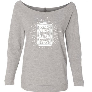May include: A light gray off-the-shoulder sweatshirt with long sleeves. The front features a white graphic of a beverage container with the text "STOP THINKING START DRINKING" in a stylized font, surrounded by radiating lines.