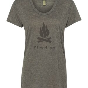 Puede incluir: Camiseta gris jaspeado con cuello redondo y un gr&aacute;fico gris oscuro de una fogata y las palabras "fired up" impresas debajo. La camiseta tiene mangas cortas y un corte holgado.