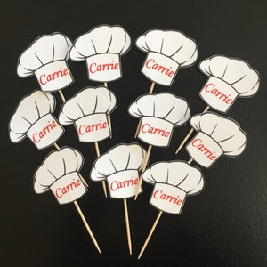 May include: Ten white chef hat cupcake toppers with the name "Carrie" printed in red on each topper.