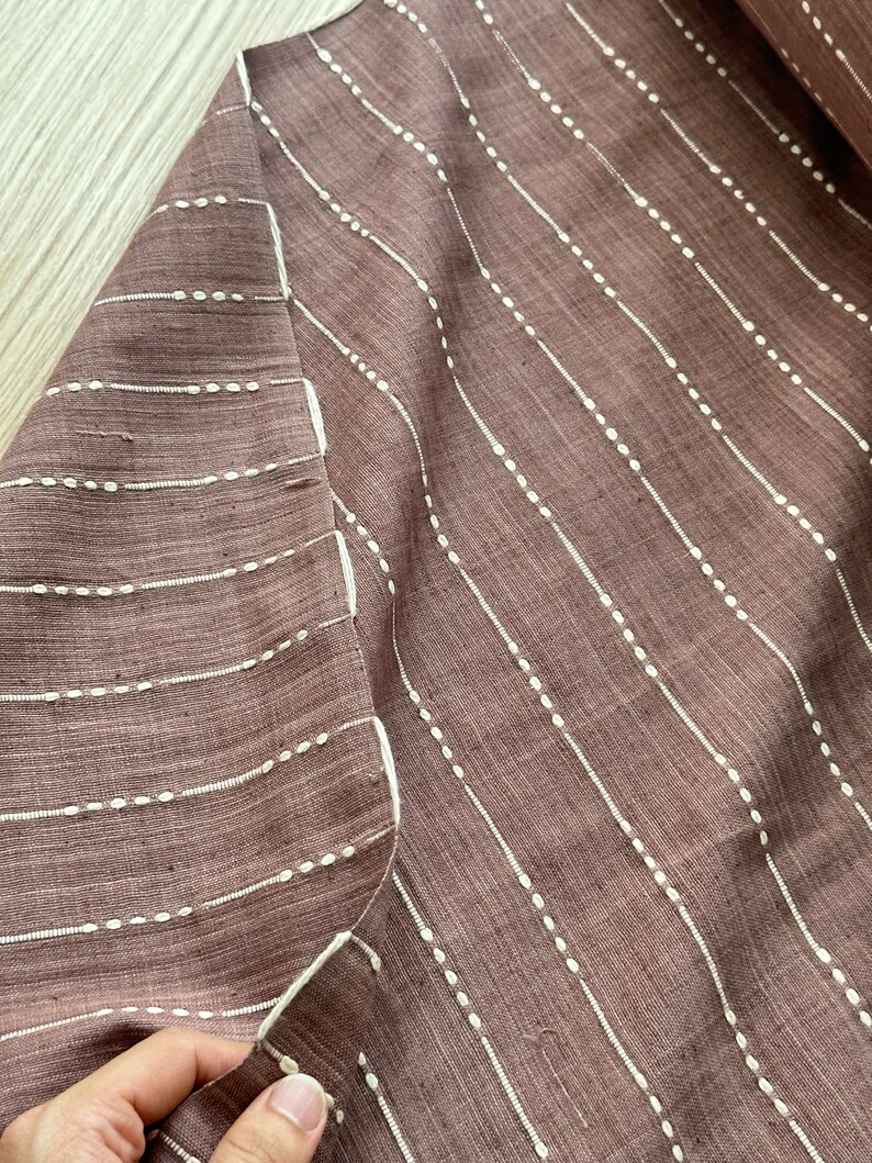 May include: A close-up of a brown fabric with white vertical stripes. The stripes are made of small white dots.