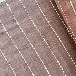 May include: A close-up of a brown fabric with white dotted lines. The fabric has a subtle texture and a slightly faded appearance.