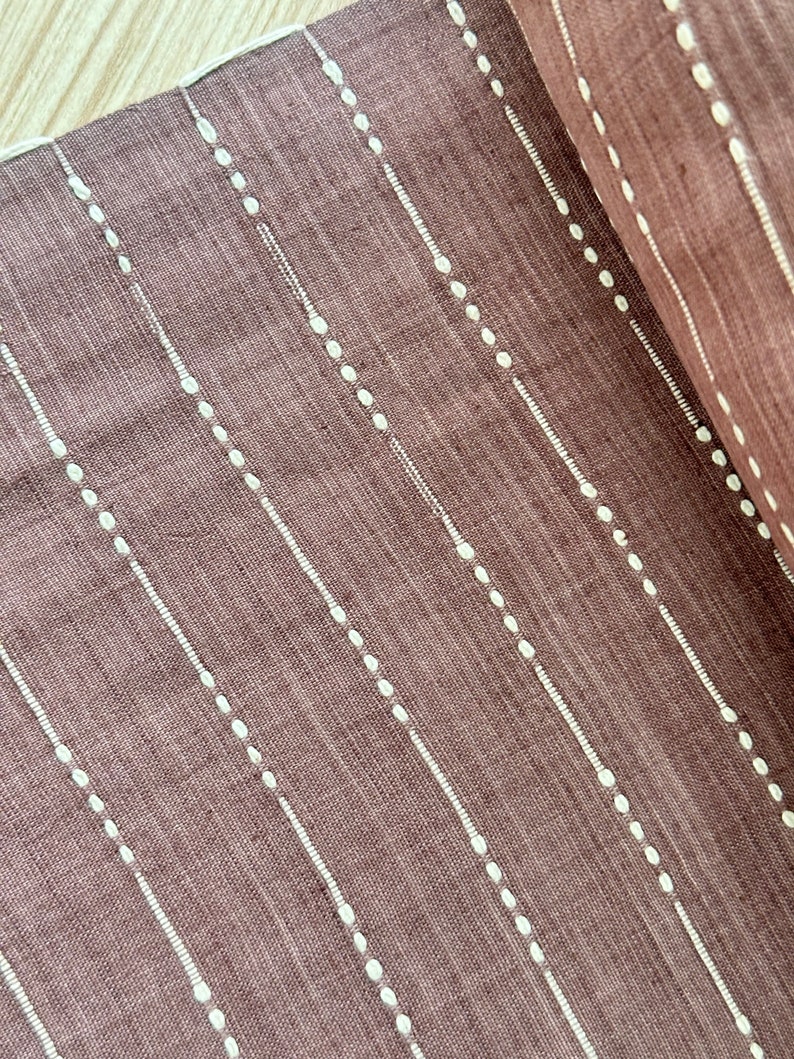 May include: A close-up of a brown fabric with white dotted lines. The fabric has a subtle texture and a slightly faded appearance.