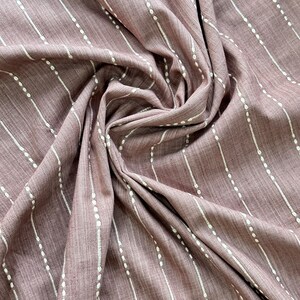 May include: A close-up of a mauve fabric with white vertical stripes and small white dots. The fabric is folded and draped, showing its texture.