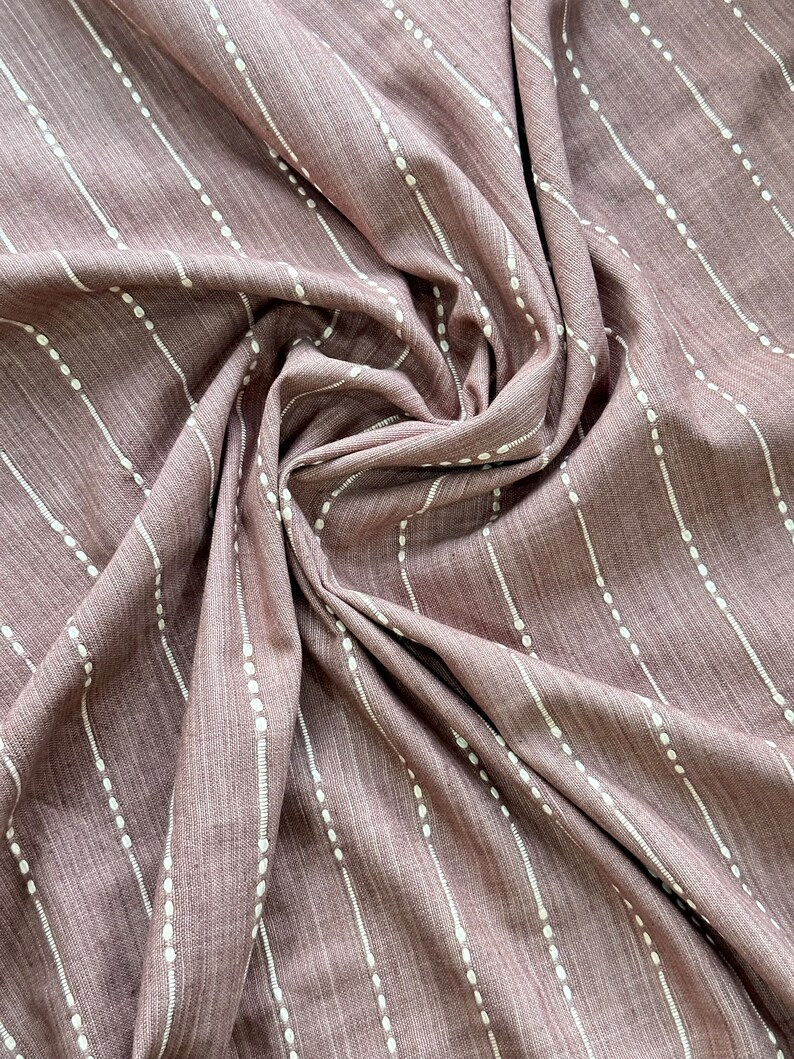 May include: A close-up of a mauve fabric with white vertical stripes and small white dots. The fabric is folded and draped, showing its texture.