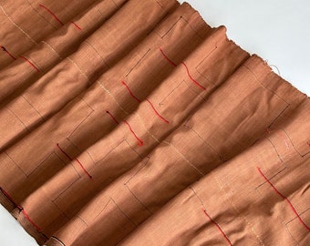 Peut inclure: Un tissu brun avec un motif géométrique de coutures rouges et dorées. Le tissu est plié et a une texture rugueuse.