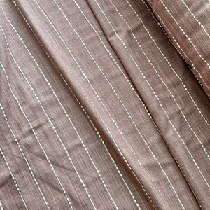 May include: A close-up of a brown fabric with white dotted lines. The fabric has a subtle texture and a soft, muted color.