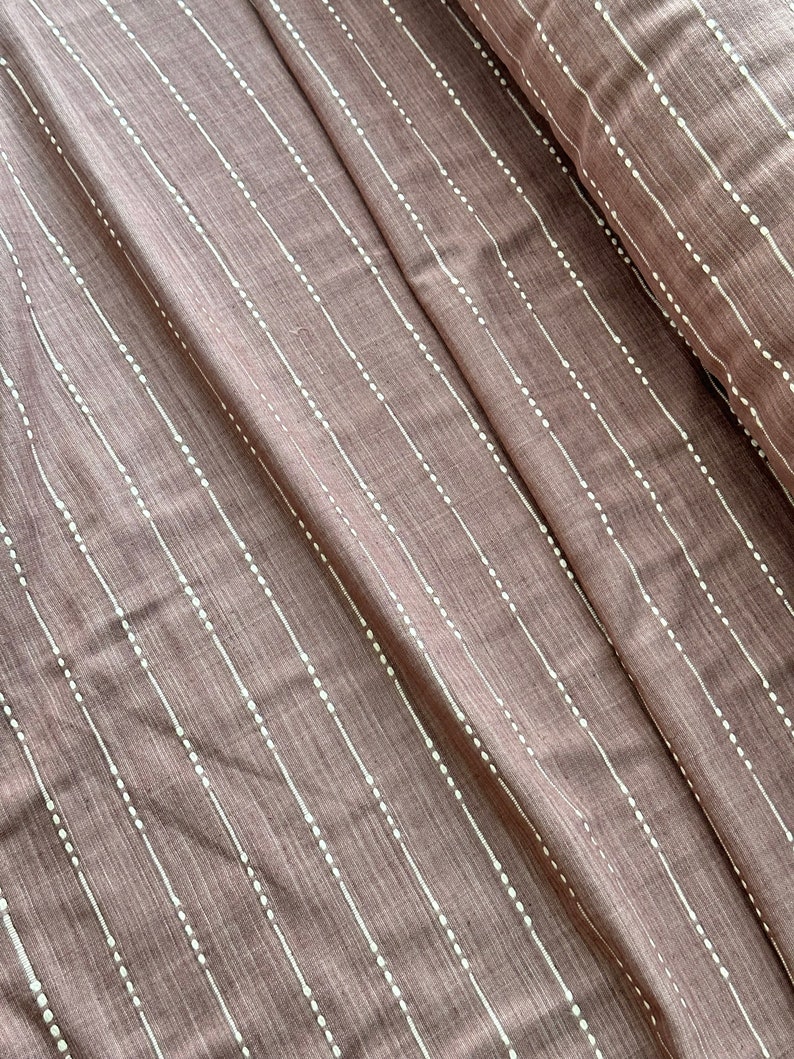 May include: A close-up of a brown fabric with white dotted lines. The fabric has a subtle texture and a soft, muted color.