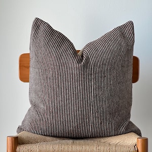 Könnte beinhalten: Ein braunes und weiß gestreiftes Kissen auf einem Holzstuhl mit einem geflochtenen Sitz.