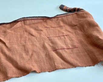 Peut inclure: Un long morceau de tissu rectangulaire de couleur brun clair avec des coutures rouges. Le tissu a une surface rugueuse et texturée et est plié en deux.
