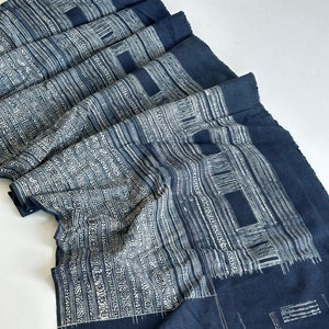 May include: A folded piece of indigo blue fabric with a white geometric pattern. The fabric is woven with a traditional design and has a slightly textured surface.