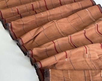 Peut inclure: Tissu brun à fines rayures noires et rouges. Le tissu est plié et présente un bord effiloché.