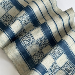 May include: A white fabric with a blue and white geometric pattern. The fabric is folded and has a rough texture.