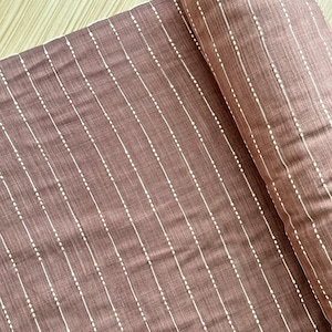 May include: A brown fabric with white vertical stripes and small white dots. The fabric is folded in half.