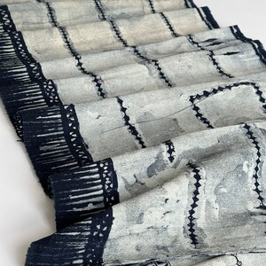 Peut inclure: Un tissu blanc avec un motif géométrique noir. Le tissu est plié et a une bordure frangée.