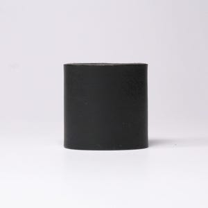 May include: A solid black, cylindrical object with a slightly textured surface. The object has a rounded rectangular shape and stands upright against a white background. The item appears to be made of a matte material.