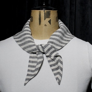 May include: A white waffle-knit shirt with a gray and white striped necktie. The necktie is tied in a knot at the front. The shirt is displayed on a mannequin.