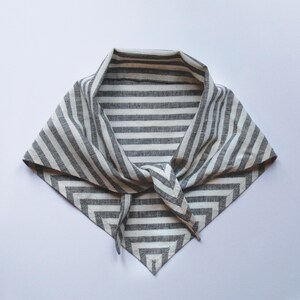 May include: A gray and white striped bandana, knotted at the front. The fabric is folded into a triangle shape, with the stripes running horizontally across the fabric. The bandana is made of a soft material.