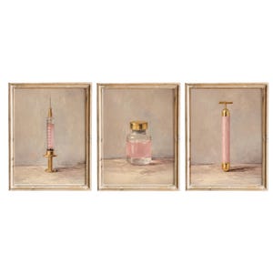 Puede incluir: Tres obras de arte enmarcadas que presentan artículos de belleza y bienestar. La primera muestra una jeringa con líquido rosa, la segunda una botella de vidrio con tapa dorada y líquido rosa, y la tercera un rodillo de jade rosa con detalles dorados.