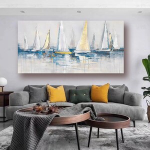May include: Abstract painting of sailboats on a blue and white water background. The sailboats are white with gold accents. The painting is framed and hanging on a wall in a living room.