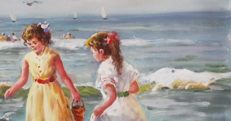May include: Two girls in summer dresses play on a beach. One girl wears a yellow dress with a red belt and holds a bucket. The other girl wears a white dress with a green sash. The ocean is in the background.