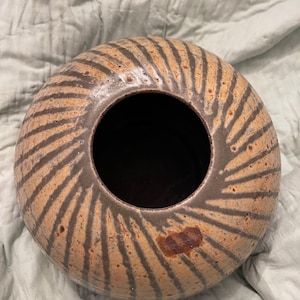 May include: A brown and black ceramic vase with a wide opening and a swirling pattern. The vase is round and has a textured surface.