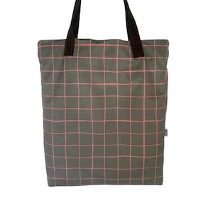 Op de afbeelding: Een grijze tote bag met een roze rasterpatroon. De tas heeft bruine handvatten en een klein label. Deze tas is ontworpen voor het dragen van spullen.