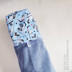 May include: A blue hooded towel with a hockey-themed print featuring hockey sticks, pucks, skates, and gloves. The towel has a blue terry cloth lining.
