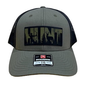 May include: A green and black trucker hat with a black patch that says "HUNT" with a silhouette of a deer and a hunter with a bow and arrow. The hat has a black mesh back and a Richardson 115 logo.