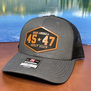 May include: A gray and black trucker hat with a brown leather patch that says "Make America 45*47 Great Again".