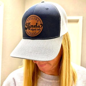 May include: A navy blue and gray trucker hat with a brown leather patch that says "Feeling Kinda idgaf-ish Today".
