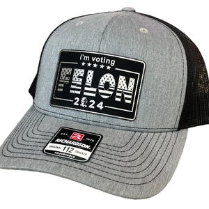 May include: A gray and black trucker hat with a black patch that says "I'm voting FELON -2024" with an American flag design. The patch has a white border and stars above the text. The hat has a black mesh back and a Richardson 112 label.
