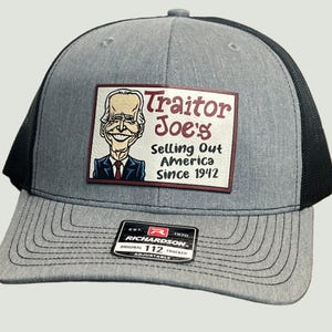May include: A gray and black trucker hat with a red, white, and blue patch that says "Traitor Joe's Selling Out America Since 1942". The patch features a cartoon image of a man with a mustache.