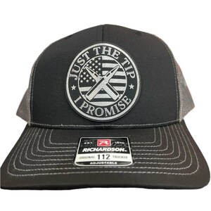 May include: Black and gray trucker hat with a black and white patch that says "Just the Tip I Promise" with a crossed bullet design and an American flag in the background. The hat has a Richardson logo and says "Original Trucker 112 Adjustable".