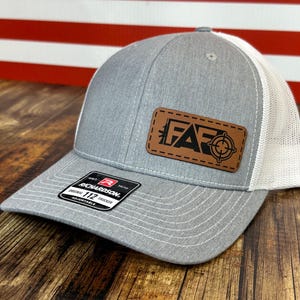 May include: A gray and white trucker hat with a brown leather patch that says "F.A.F.O." with a target symbol. The hat is adjustable and has a Richardson 112 label.