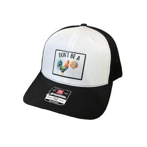 May include: White and black trucker hat with a rooster and lollipop graphic and the text "Don't be a".