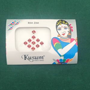 May include: A package of red and gold decorative bindi stickers with the brand name "Kusum Fancy Bindi" and the text "Rim Zim".