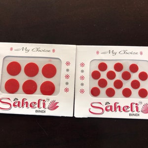 May include: Two packages of red round bindi stickers. Each package has the text "My Choice" and "Saheli Bindi" printed on it.