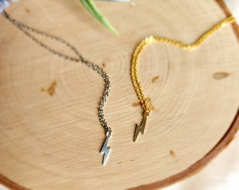 May include: Two delicate necklaces with lightning bolt charms. One necklace is silver and the other is gold. The necklaces are displayed on a wooden surface.