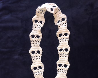 May include: A white crocheted scarf with a repeating pattern of skull shapes.