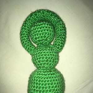 May include: A green crocheted figurine shaped like a woman with a round head and a long, pointed body.