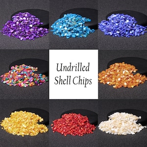 Puede incluir: Surtido de virutas de concha sin taladrar en varios colores, incluyendo morado, azul, multicolor, naranja, amarillo, rojo y blanco. Las virutas de concha se muestran sobre superficies negras.