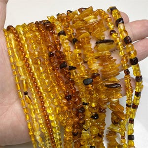 Puede incluir: Una colección de collares de ámbar en varios estilos y tonos de amarillo y marrón. Los collares presentan cuentas de diferentes formas y tamaños, incluyendo esferas pulidas, astillas irregulares y bloques rectangulares. Algunas cuentas son translúcidas, otras opacas.
