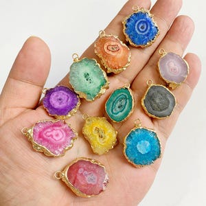 Peut inclure: Une collection de pendentifs en pierre polie colorée avec des bordures en métal doré. Les pendentifs présentent une variété de couleurs, notamment le bleu, le vert, le violet, le rose, l'orange et le jaune. Chaque pendentif a une petite boucle.