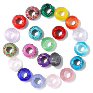 Peut inclure: Une collection de perles colorées en forme de donut, de différentes couleurs et motifs. Les perles comprennent du rouge, du vert, du jaune, de l'orange, du bleu, du violet et du transparent, certaines présentant des motifs marbrés ou texturés. Les perles sont disposées en cercle.