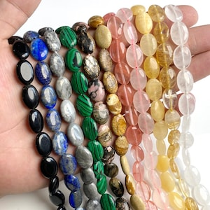 Puede incluir: Cadenas de cuentas de piedras preciosas ovaladas en varios colores, incluyendo negro, azul, verde, rosa y amarillo. Las cuentas están ensartadas, mostrando una variedad de texturas y patrones. Ideal para la fabricación de joyas o manualidades.